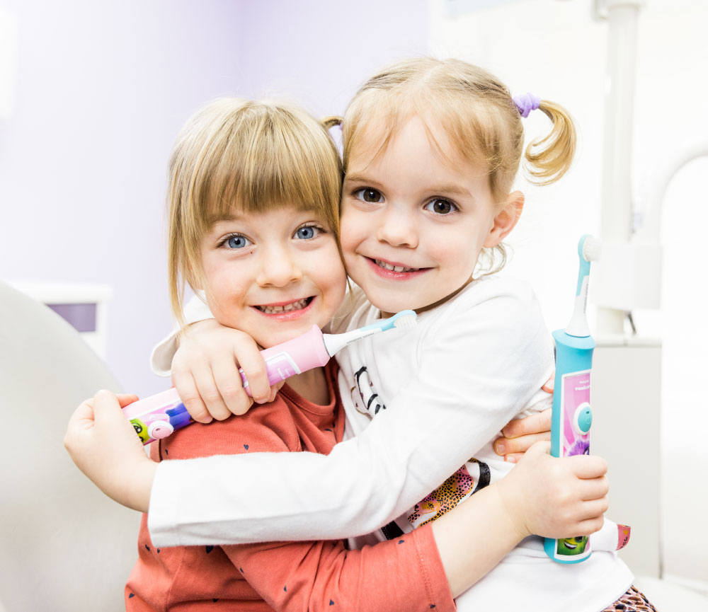 Zwei Kinder halten elektrische Zahnbürsten und umarmen sich